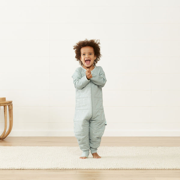 small kid wearing sage coloured onesie happily clapping